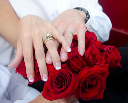 Руки жениха и невесты с букетом красных роз